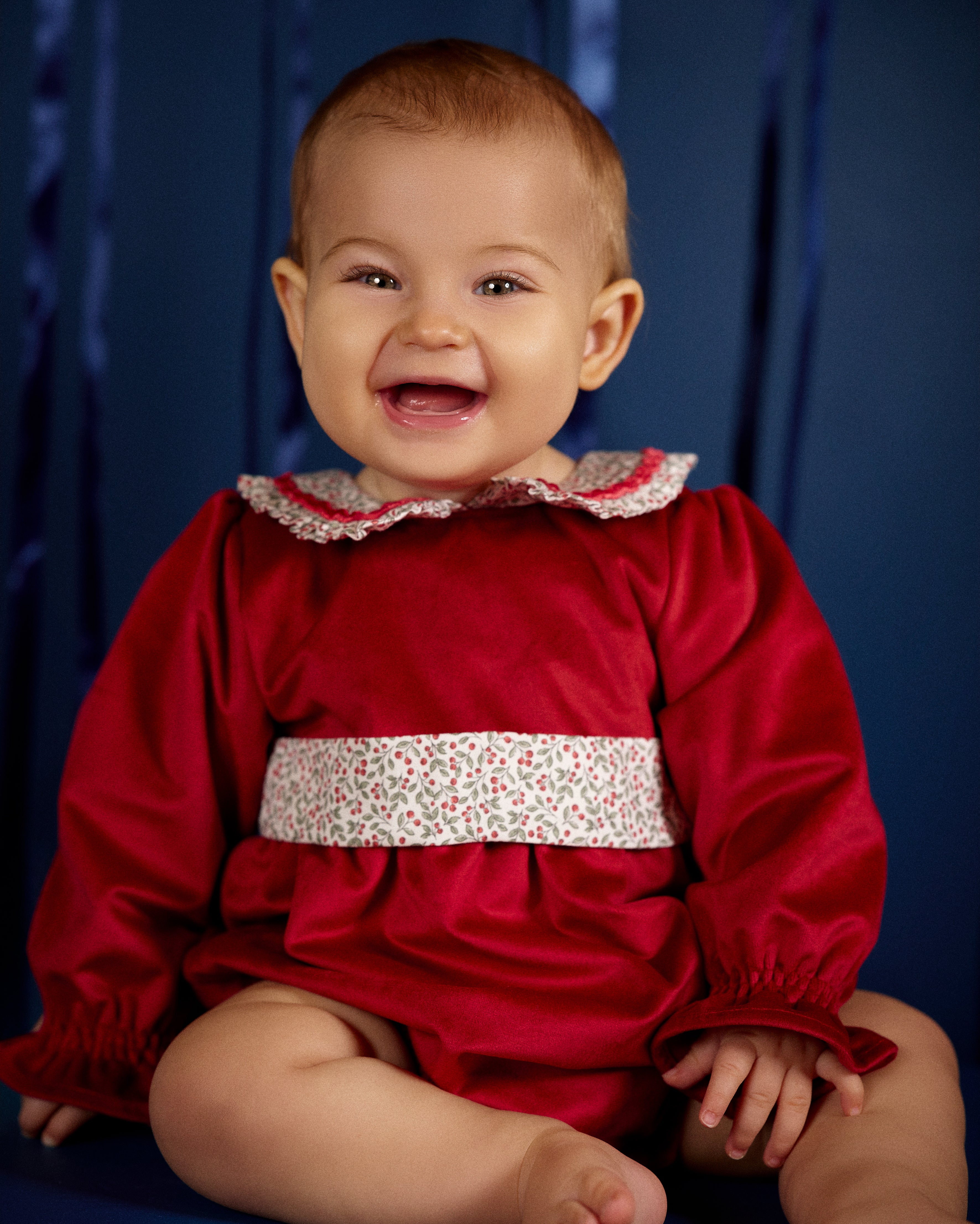 Smiling baby girl wearing Deolinda Frosty red festive baby’s first Christmas romper