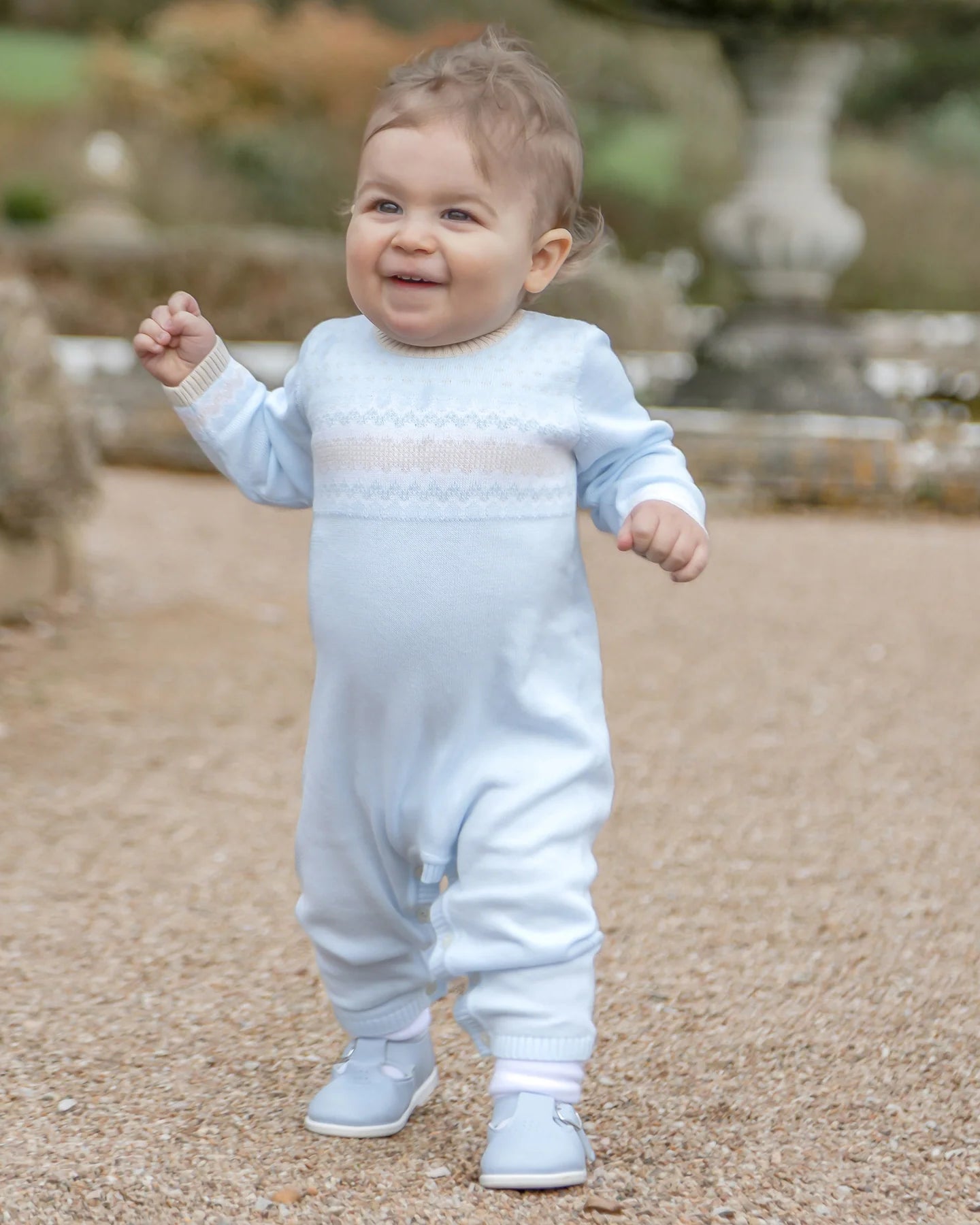 Baby boy wearing Emile et Rose Magnus blue knitted all-in-one babygrow outdoors