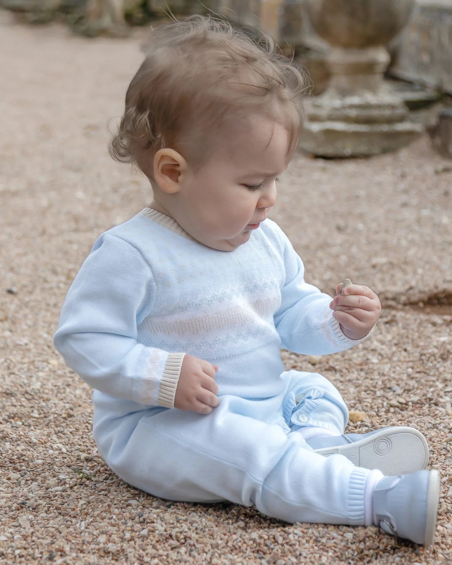 Baby boy wearing Emile et Rose Magnus blue knitted all-in-one outdoors