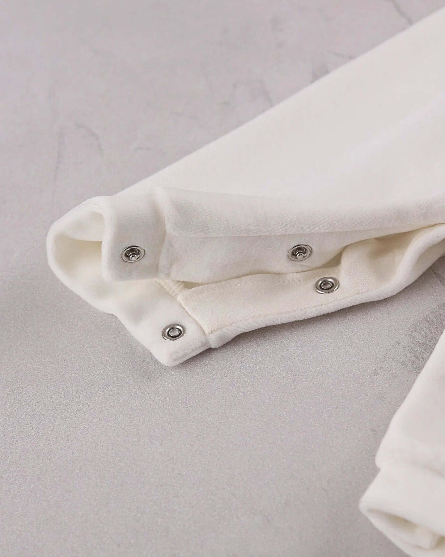 Close-up of the soft ivory velour easy access leg poppers on the Emile et Rose Marshall romper