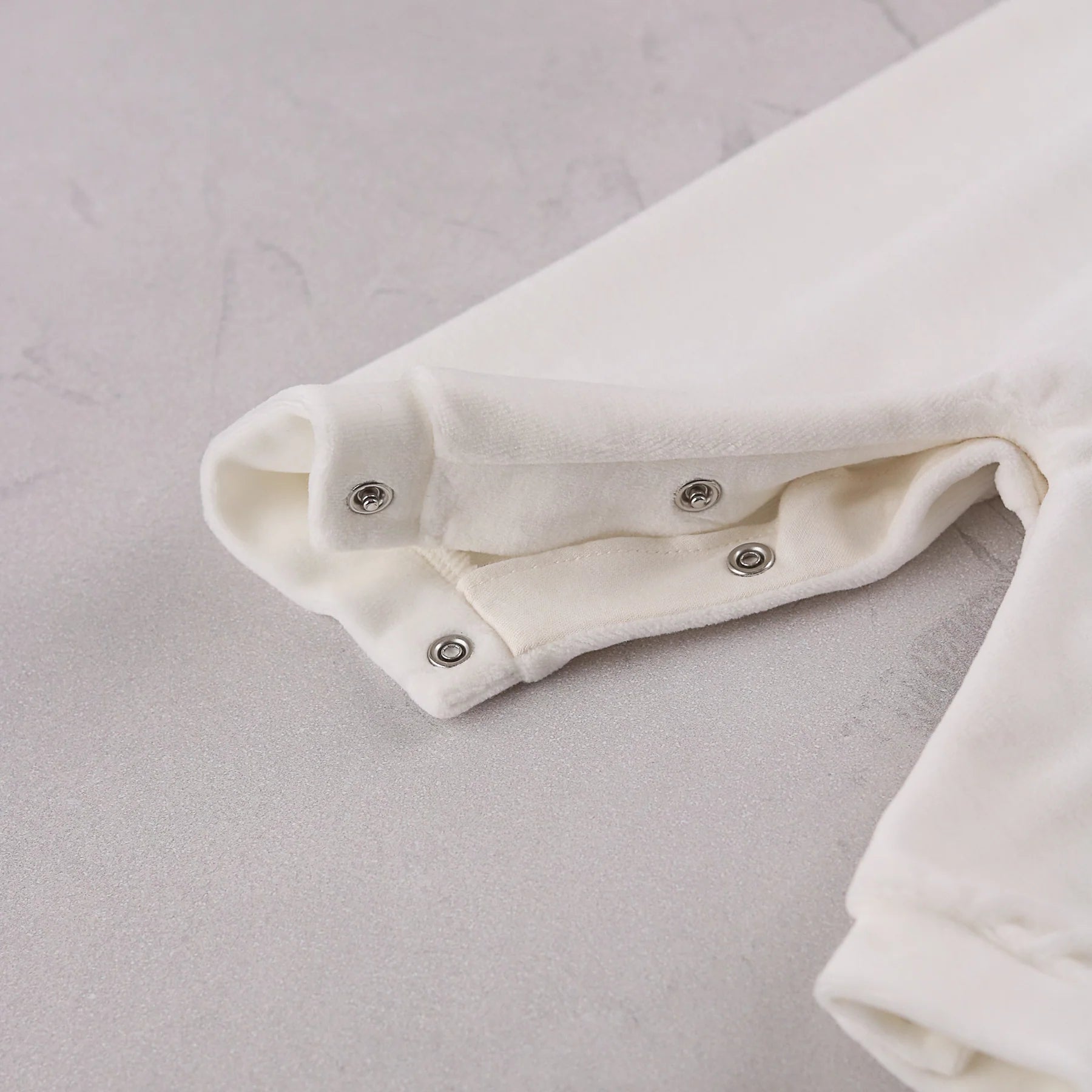 Close-up of the soft ivory velour easy access leg poppers on the Emile et Rose Marshall romper