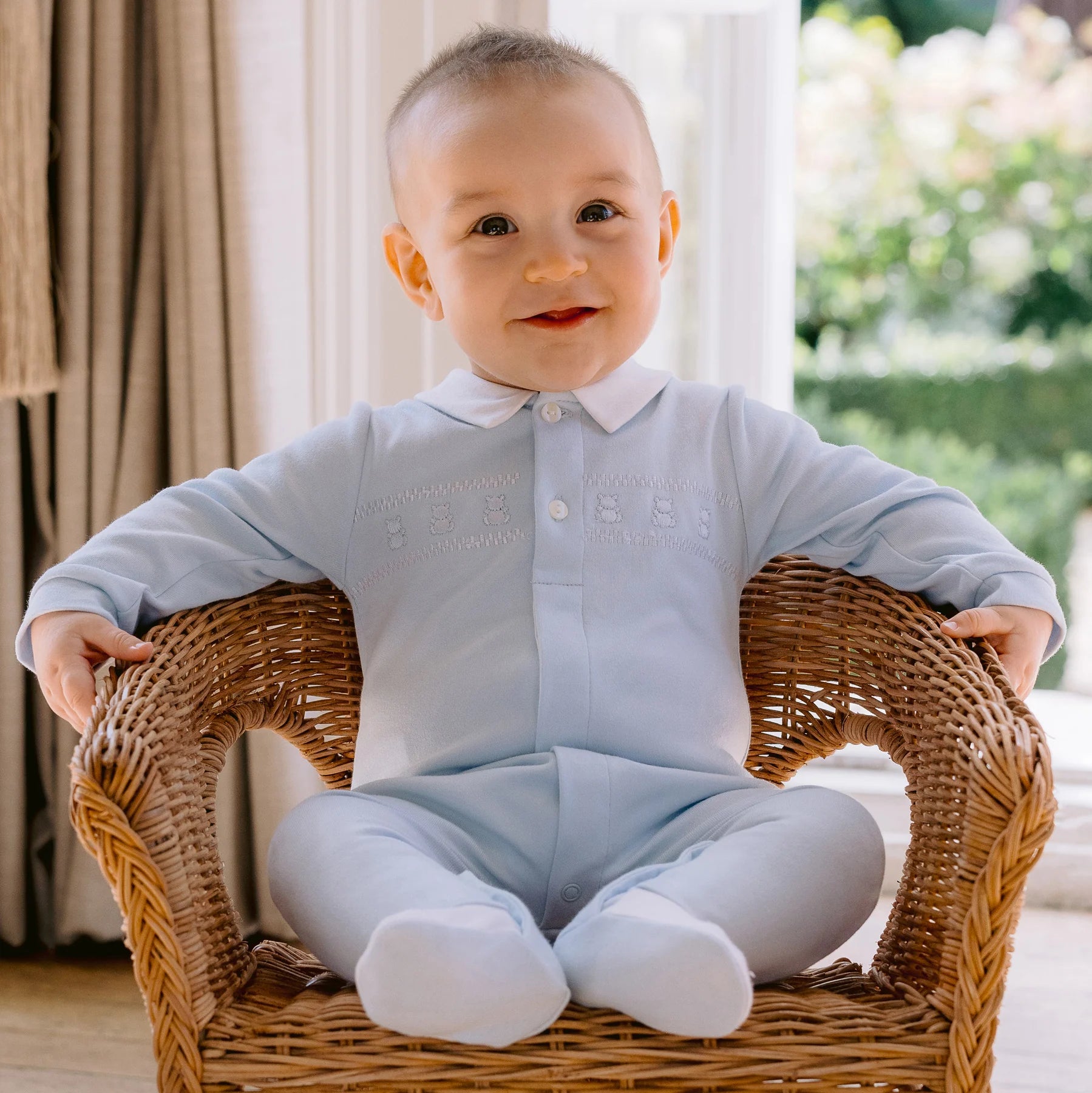 Baby boy sitting in chair wearing Emile et Rose Fisher blue babygrow with collar