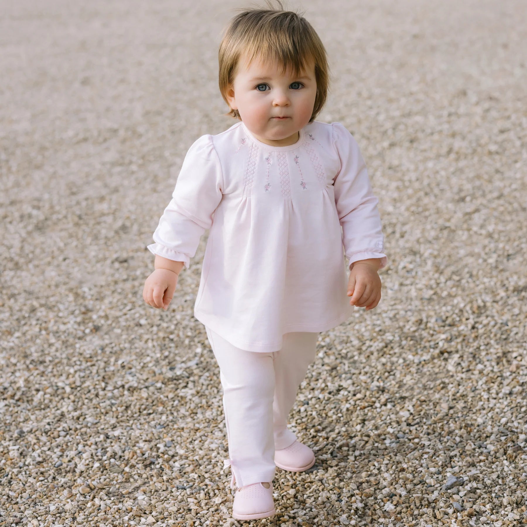 Baby girl walking outside in Emile et Rose Kate pink top and trousers set.
