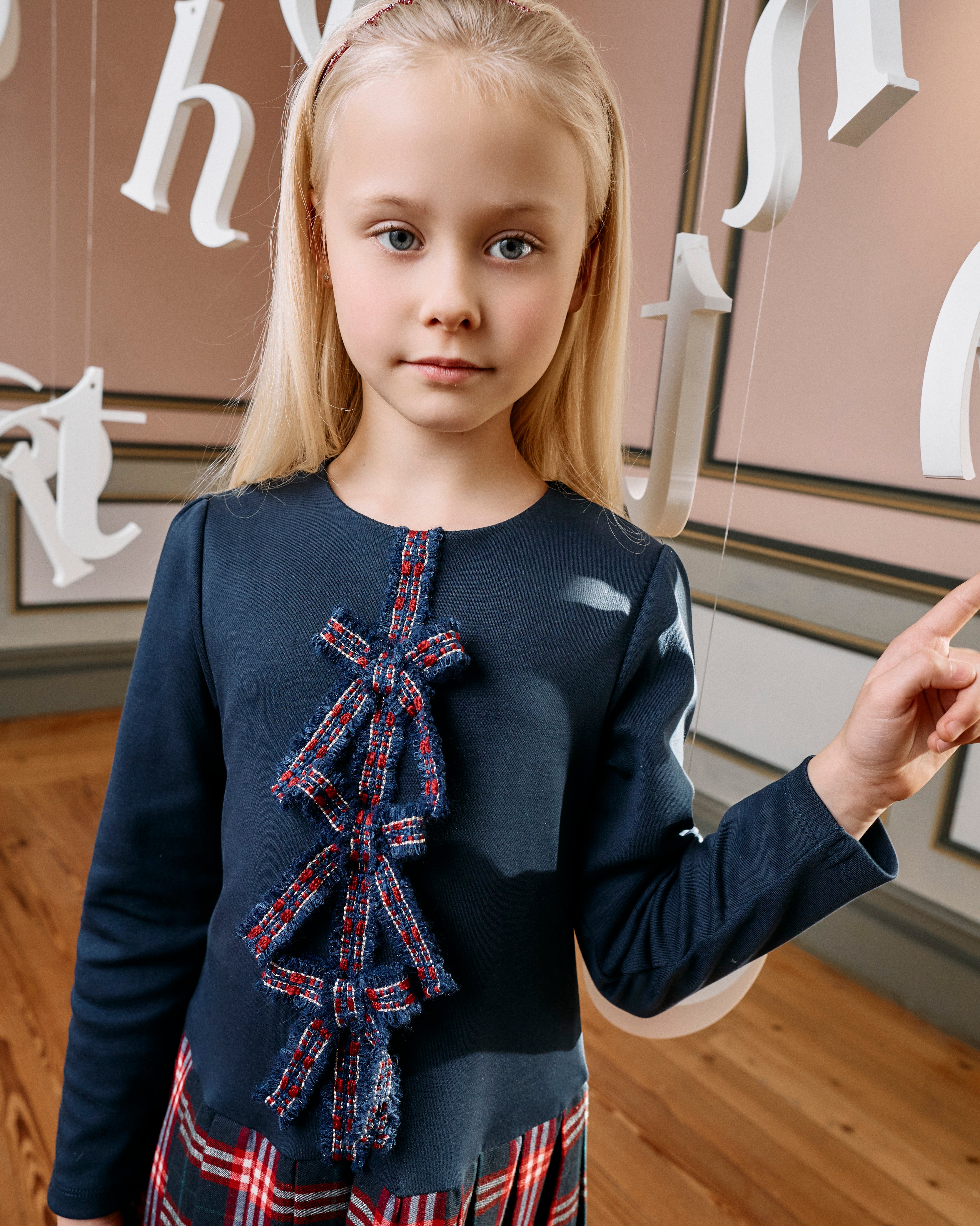Girl wearing Patachou navy tartan Christmas dress with statement bows