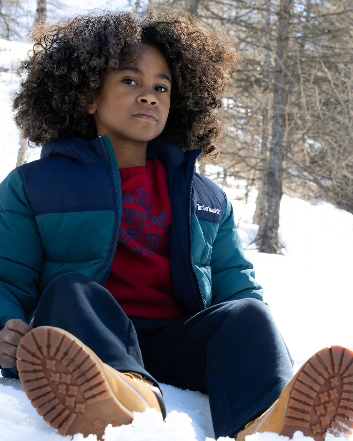 Boy wearing Timberland blue hooded puffer jacket outdoors in snowy weather