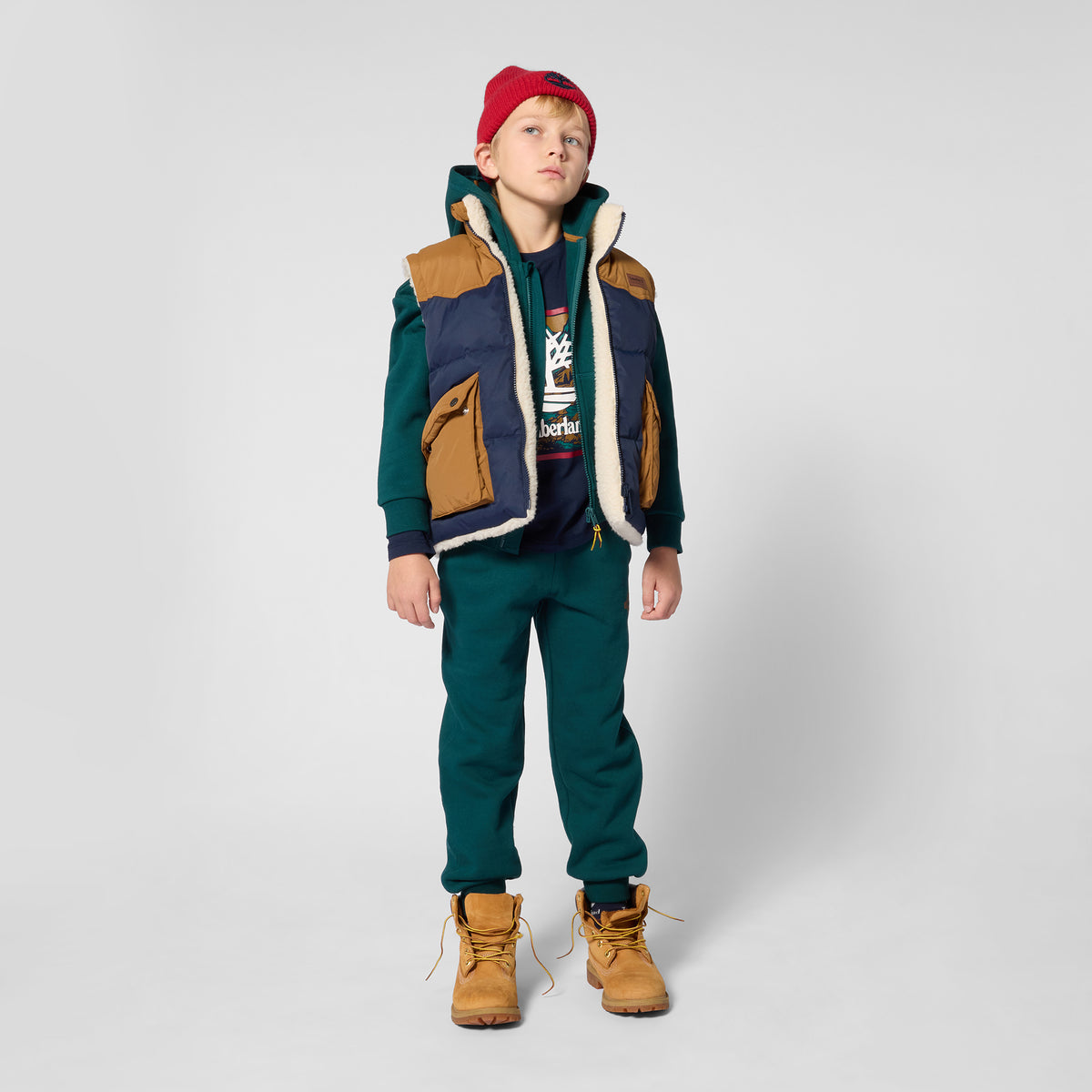 Boy wearing Timberland navy logo T-shirt with green trousers, padded gilet and tan boots