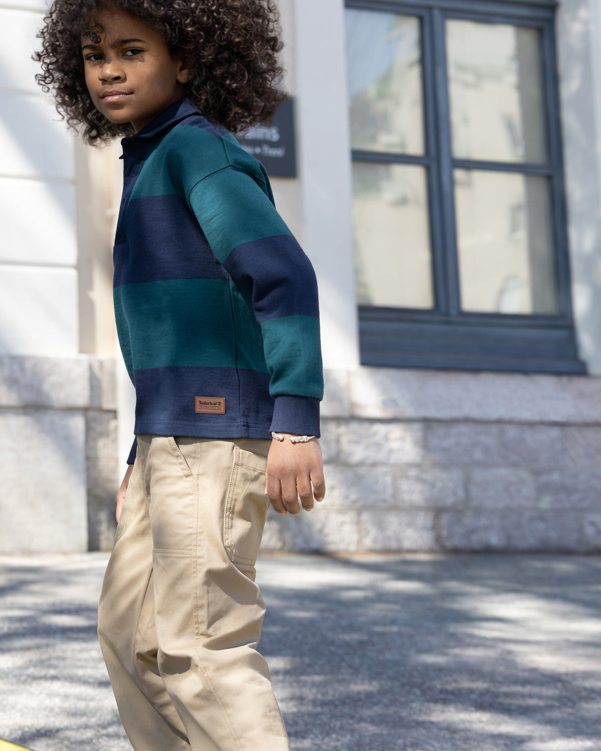 Boy wearing Timberland navy and green striped rugby shirt with beige trousers