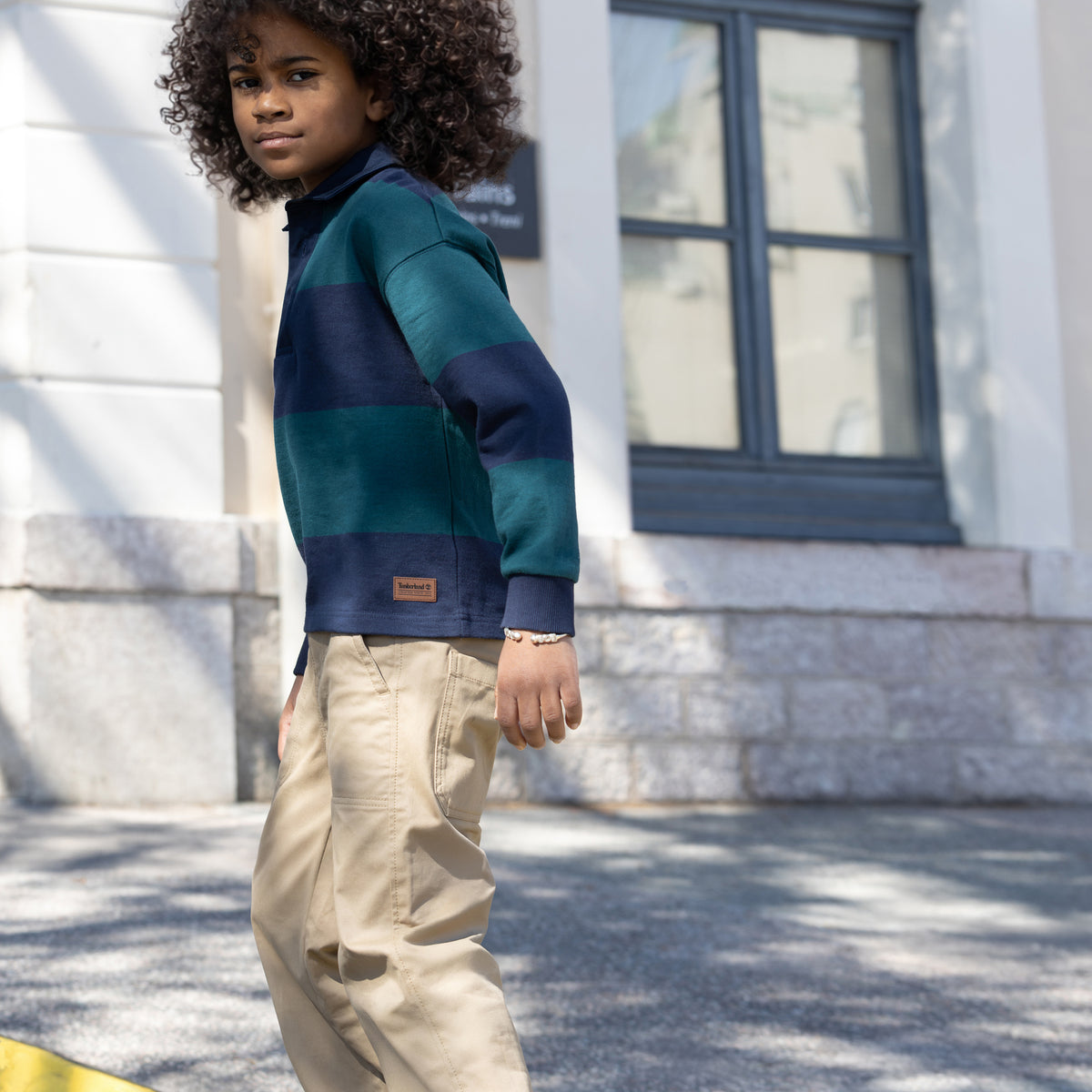 Boy wearing Timberland navy and green striped rugby shirt with beige trousers