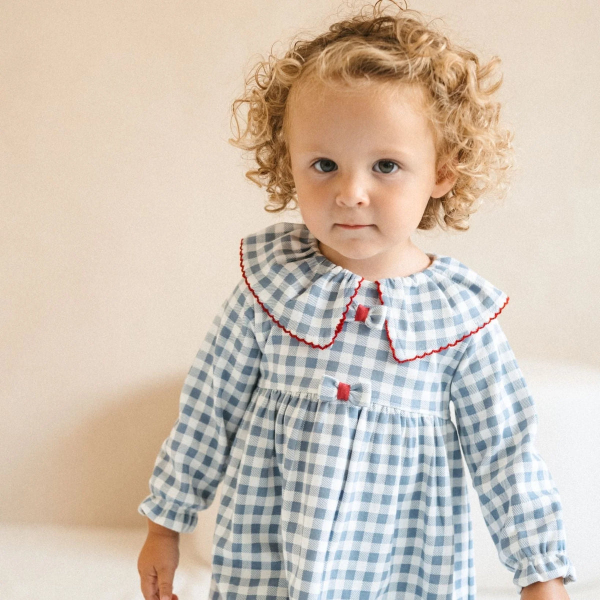 Baby girl wearing Tutto Piccolo indigo gingham dress with ruffle collar