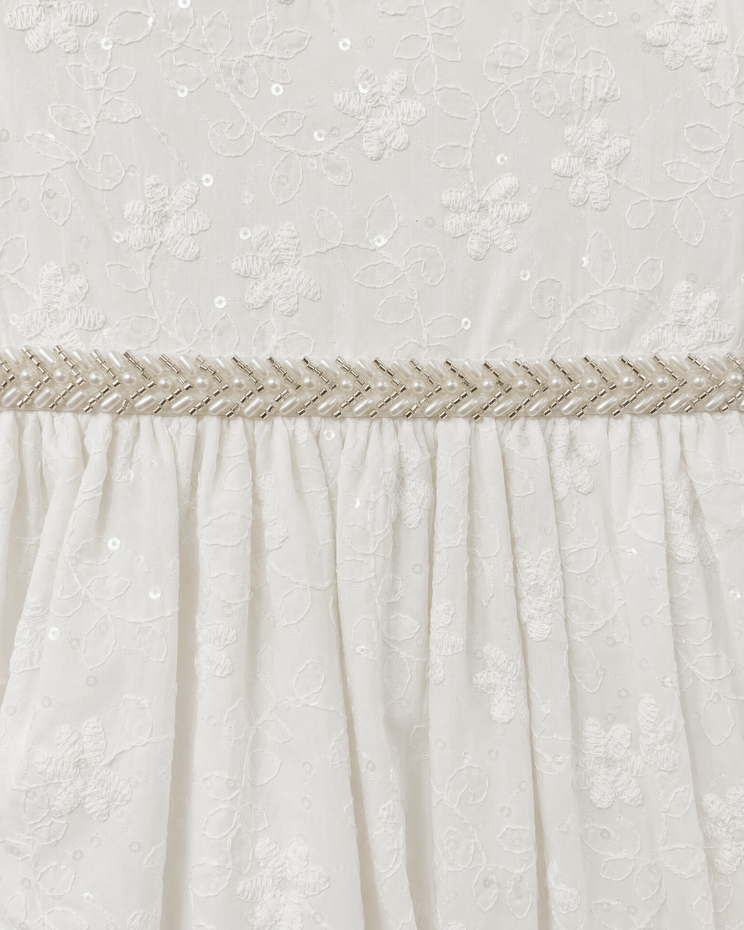 Close-up of the embroidered floral fabric and beaded waist trim on the Visara pale ivory christening gown