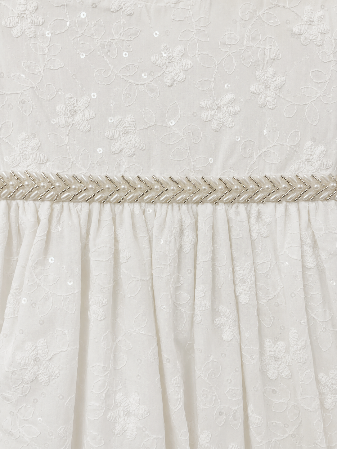 Close-up of the embroidered floral fabric and beaded waist trim on the Visara pale ivory christening gown
