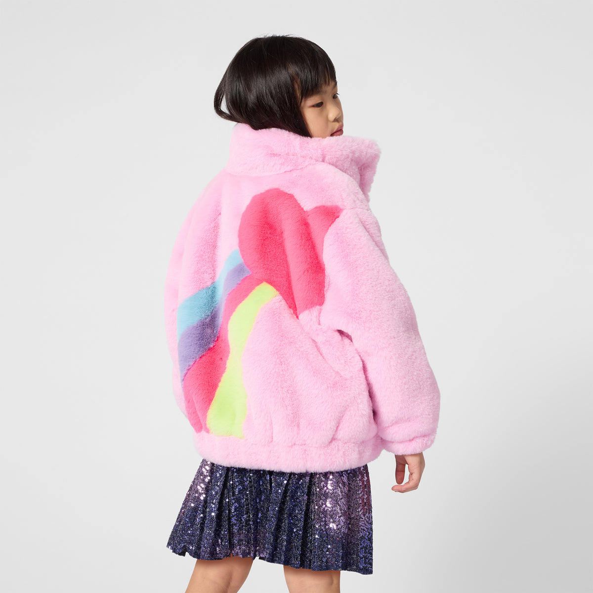 Billieblush girls pink fluffy rainbow coat worn with a navy skirt – back view