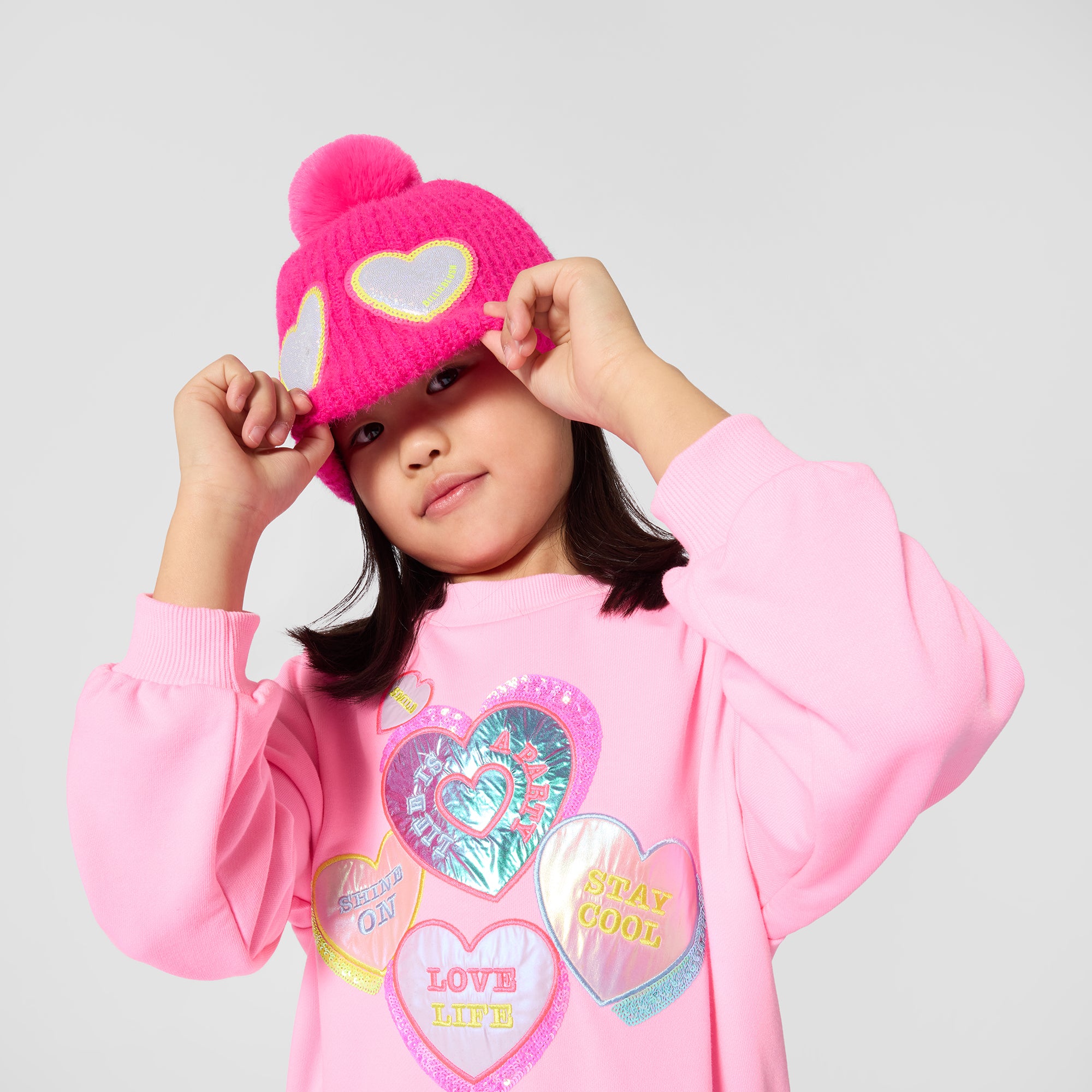 Girl modelling Billieblush pink heart print dress with blue pleated skirt