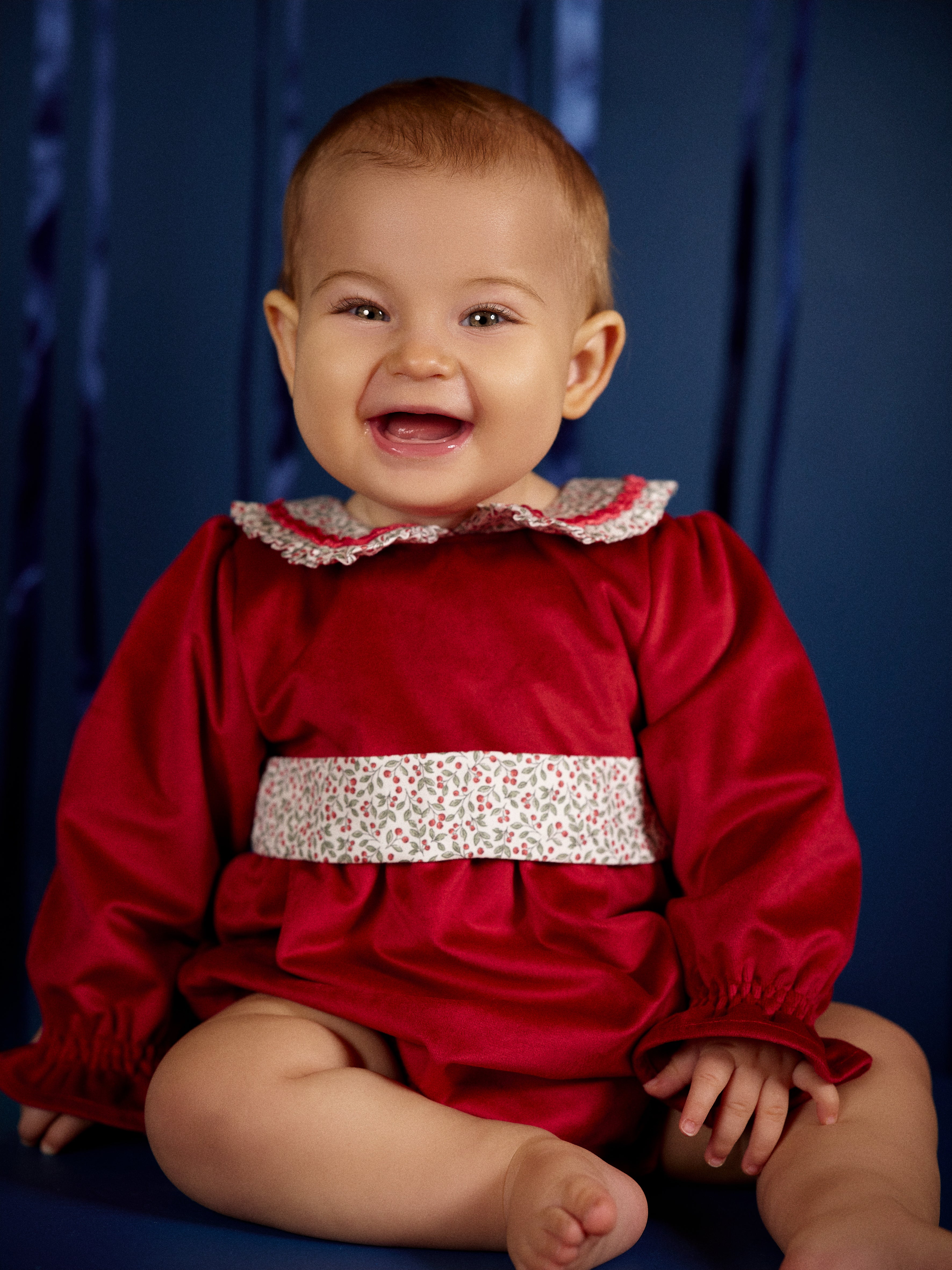 Smiling baby girl wearing Deolinda Frosty red festive baby’s first Christmas romper