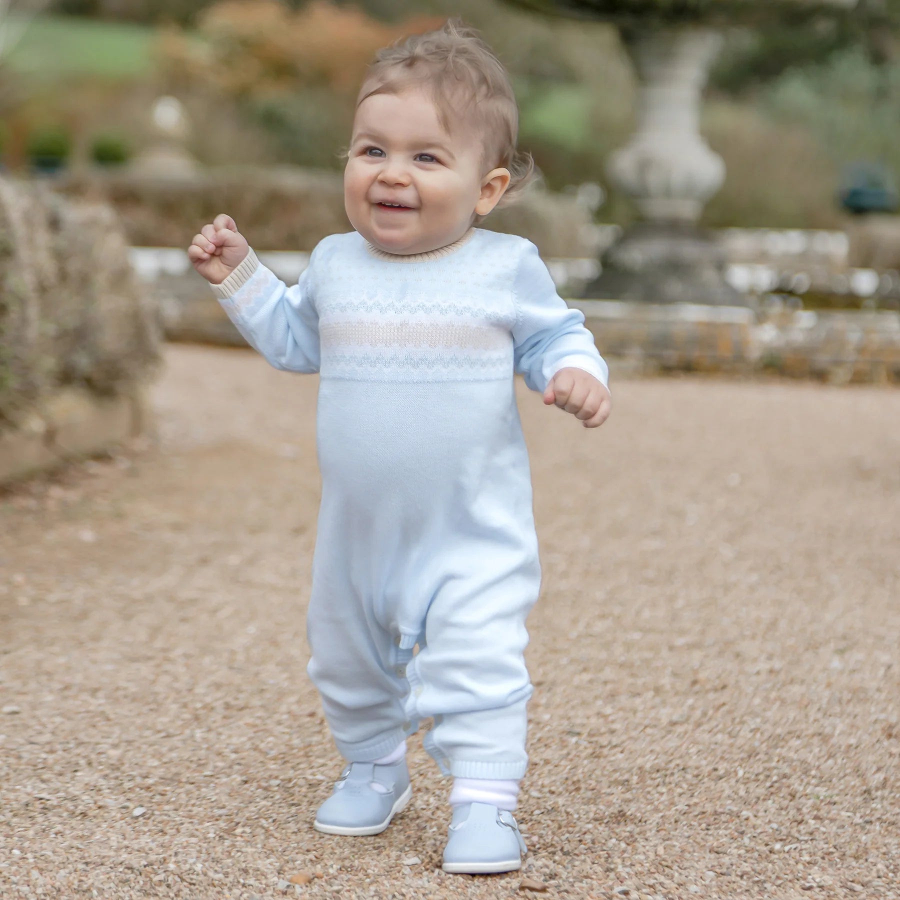 Baby boy wearing Emile et Rose Magnus blue knitted all-in-one babygrow outdoors