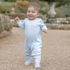 Baby boy wearing Emile et Rose Magnus blue knitted all-in-one babygrow outdoors