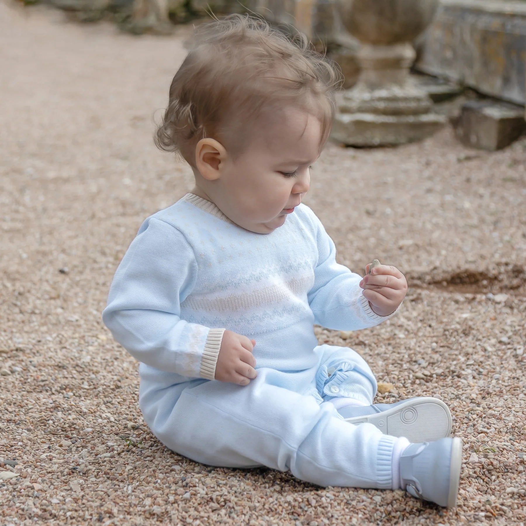 Baby boy wearing Emile et Rose Magnus blue knitted all-in-one outdoors