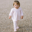 Baby girl walking outside in Emile et Rose Kate pink top and trousers set.