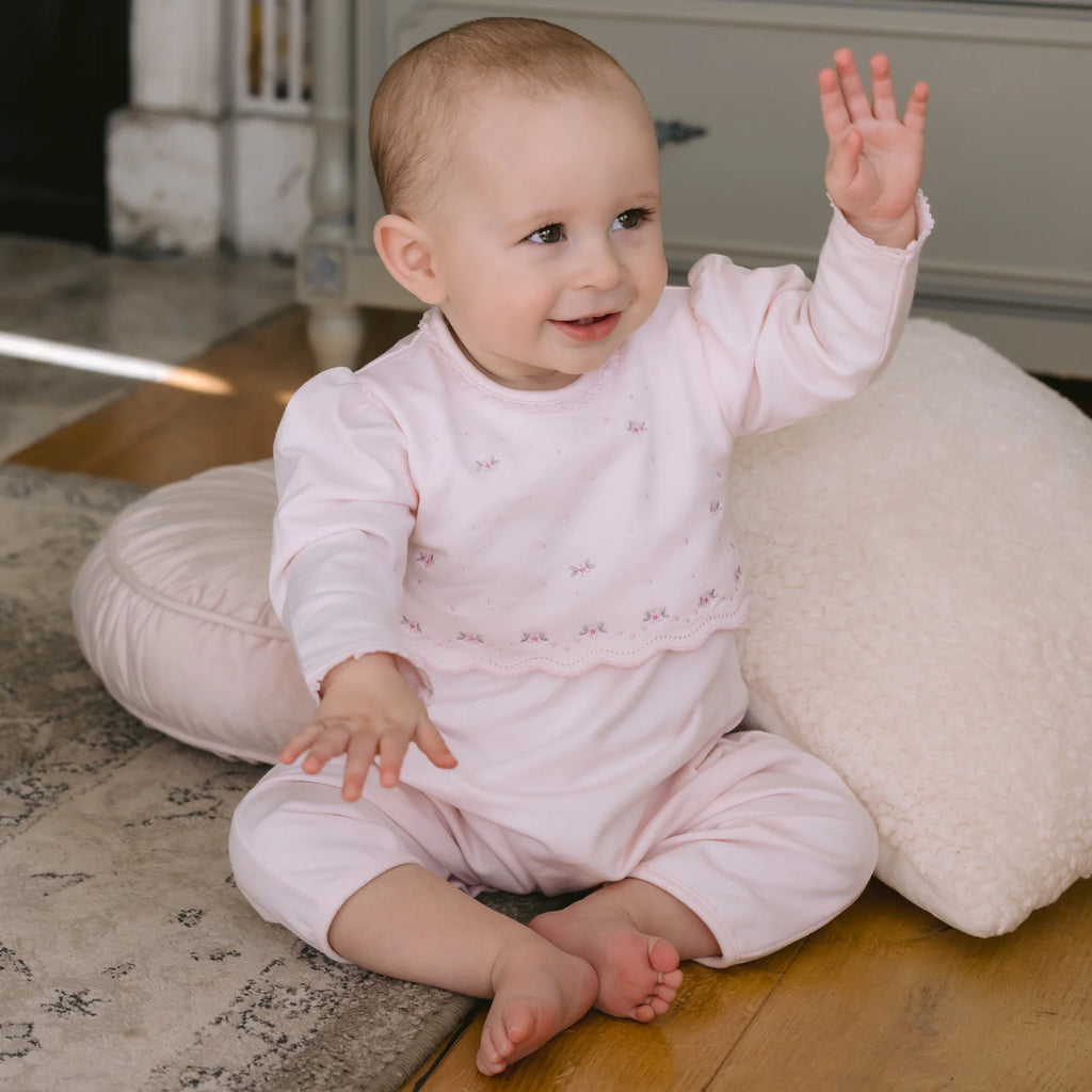 Baby girl sitting and raising hand in Emile et Rose Katerina pink babygrow.