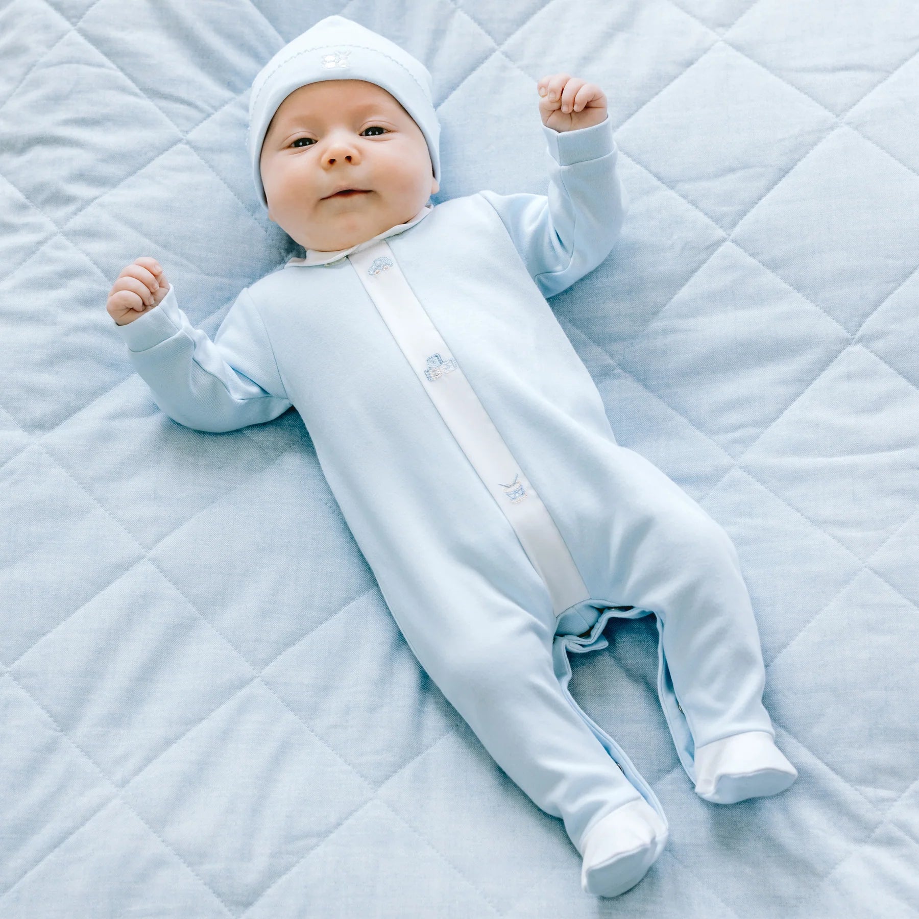 Baby wearing Emile et Rose Kent babygrow with matching hat, full-length view.