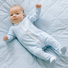 Baby boy lying down in Emile et Rose Kent blue embroidered babygrow.