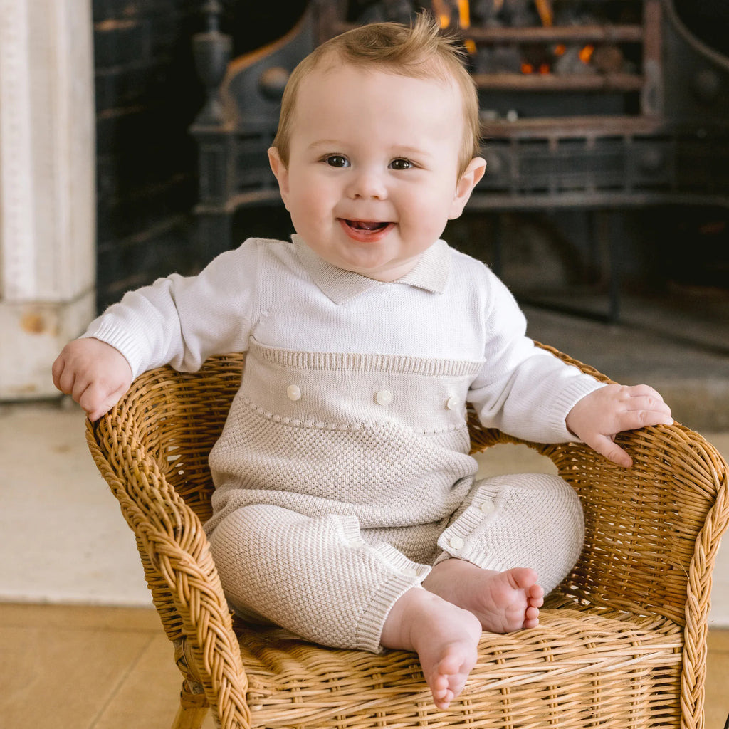 Baby boy in Emile et Rose Kenzie stone knitted babygrow sitting in a wicker chair