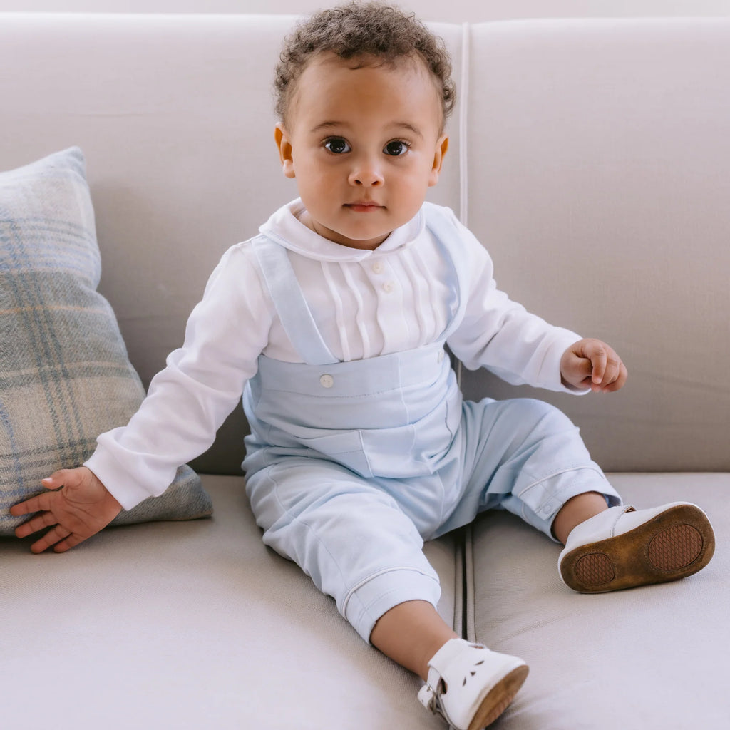 Baby boy wearing Emile et Rose Kingsley dungaree-style babygrow, sitting on chair.