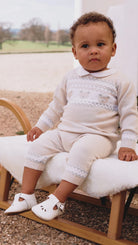 	Baby sitting outdoors in Emile et Rose Kipling knitted teddy outfit set.