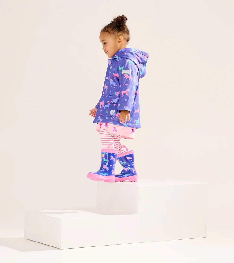 Child wearing Hatley Girls Hearts & Horses raincoat with matching purple boots 