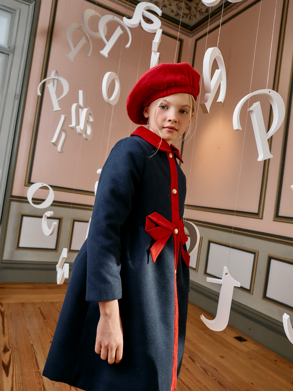Girl wearing Patachou Marine navy coat with red collar and bow detail