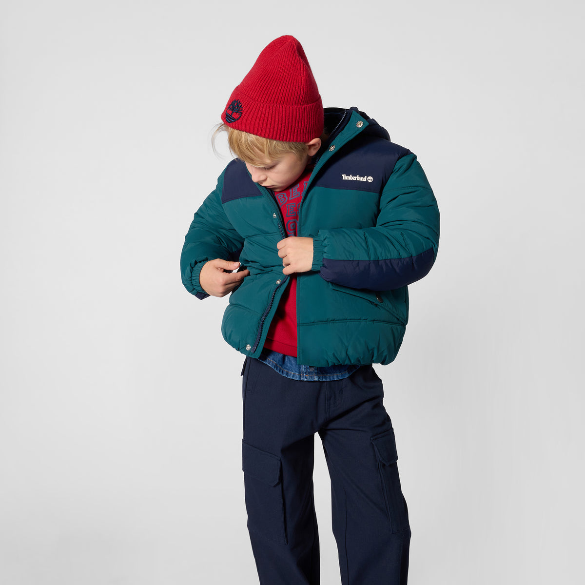 Boy wearing Timberland dark sea blue hooded puffer jacket with navy trousers
