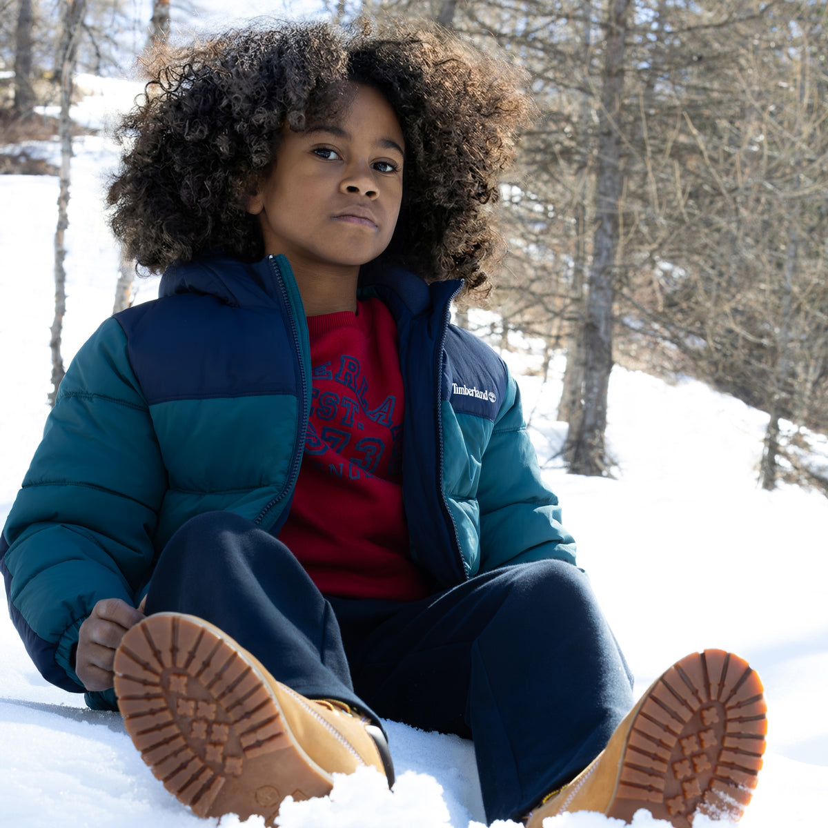 Boy wearing Timberland blue hooded puffer jacket outdoors in snowy weather