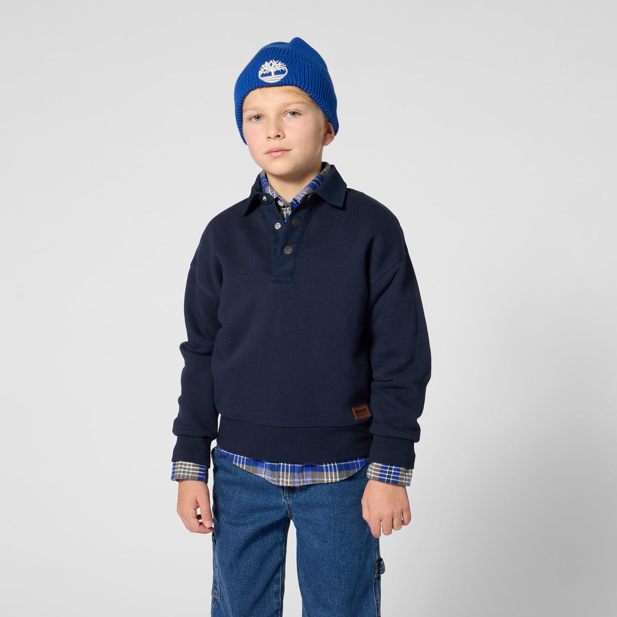 Boy wearing Timberland boys navy collared sweatshirt layered over a checked shirt