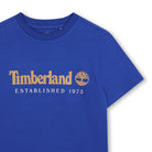 Close-up of Timberland boys blue T-shirt with gold logo and Established 1973 print