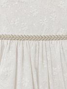 Close-up of the embroidered floral fabric and beaded waist trim on the Visara pale ivory christening gown